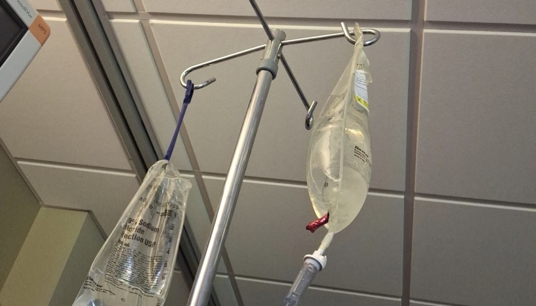 Two medical IV fluid bags hanging from a metal IV pole in a hospital room.
