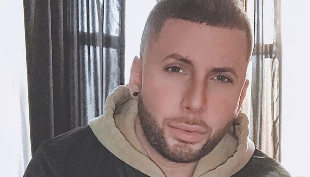 Close-up portrait of a man with short hair, a trimmed beard, and black stud earring wearing a hooded sweatshirt.