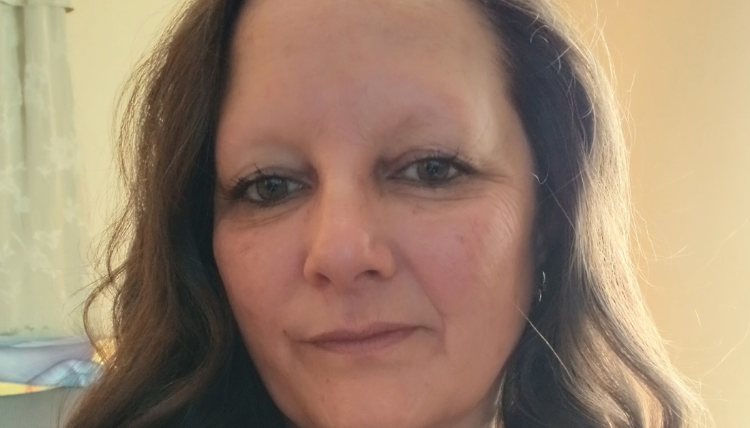 Close-up portrait of a woman with long wavy dark hair looking directly at the camera.
