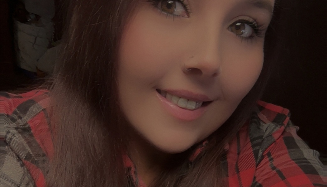 Close-up portrait of a smiling woman with brown eyes and long hair, wearing a red plaid flannel shirt.