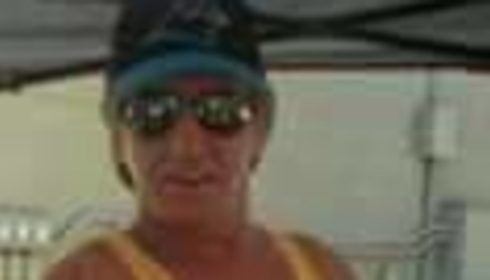 A man wearing sunglasses, a hat, and a yellow shirt outdoors.