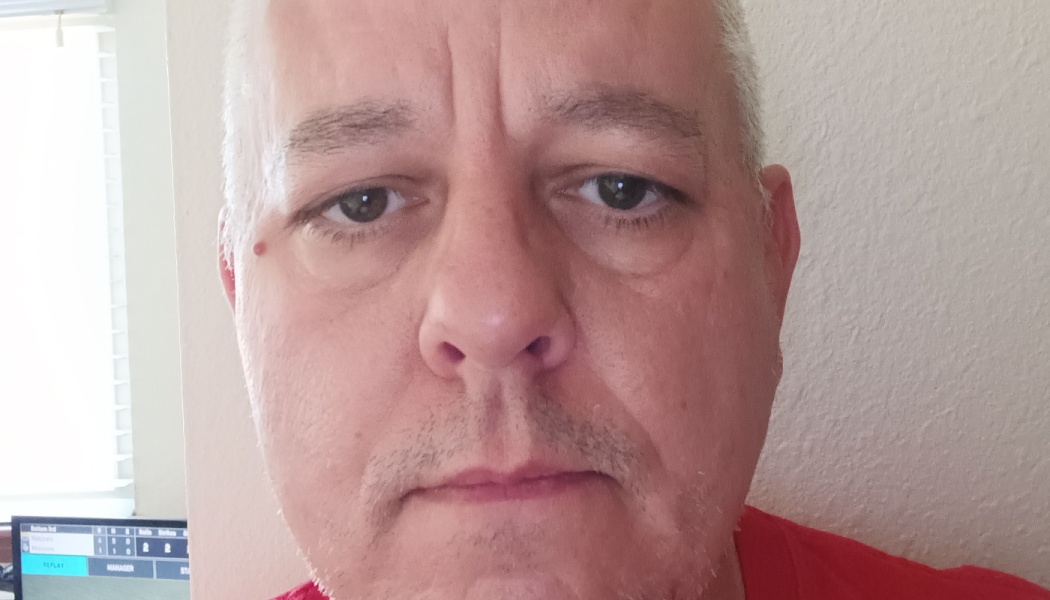 Close-up portrait of a middle-aged man with short gray hair, brown eyes, and a red shirt.