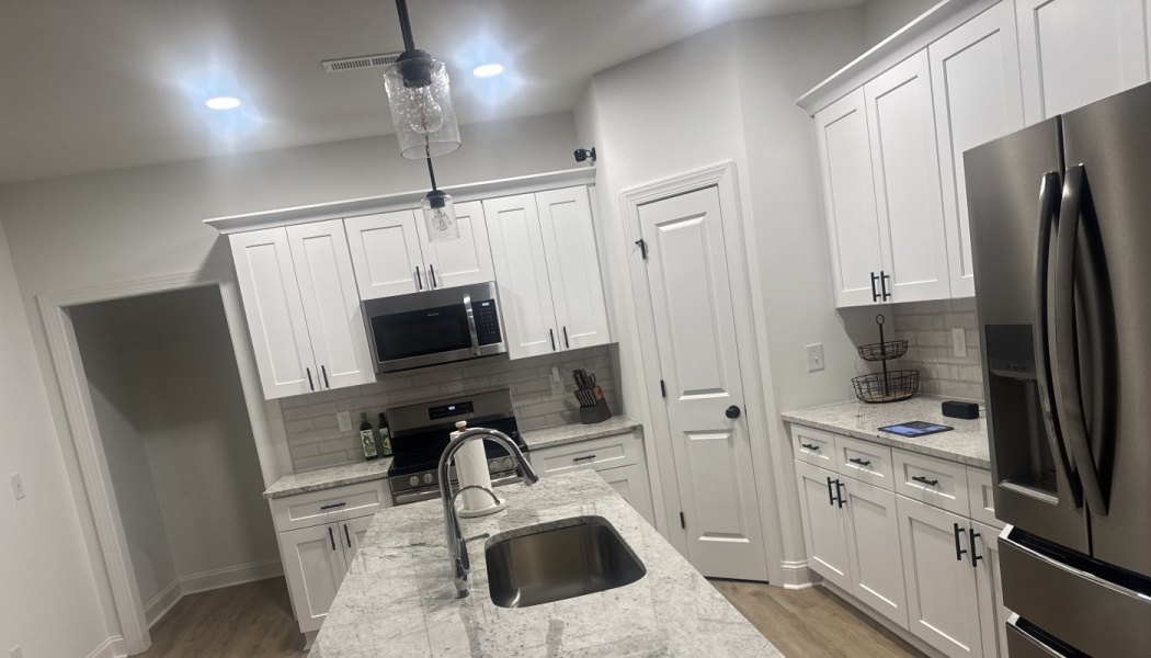 Modern kitchen featuring white cabinets, a granite island with an undermount sink, and stainless steel appliances.