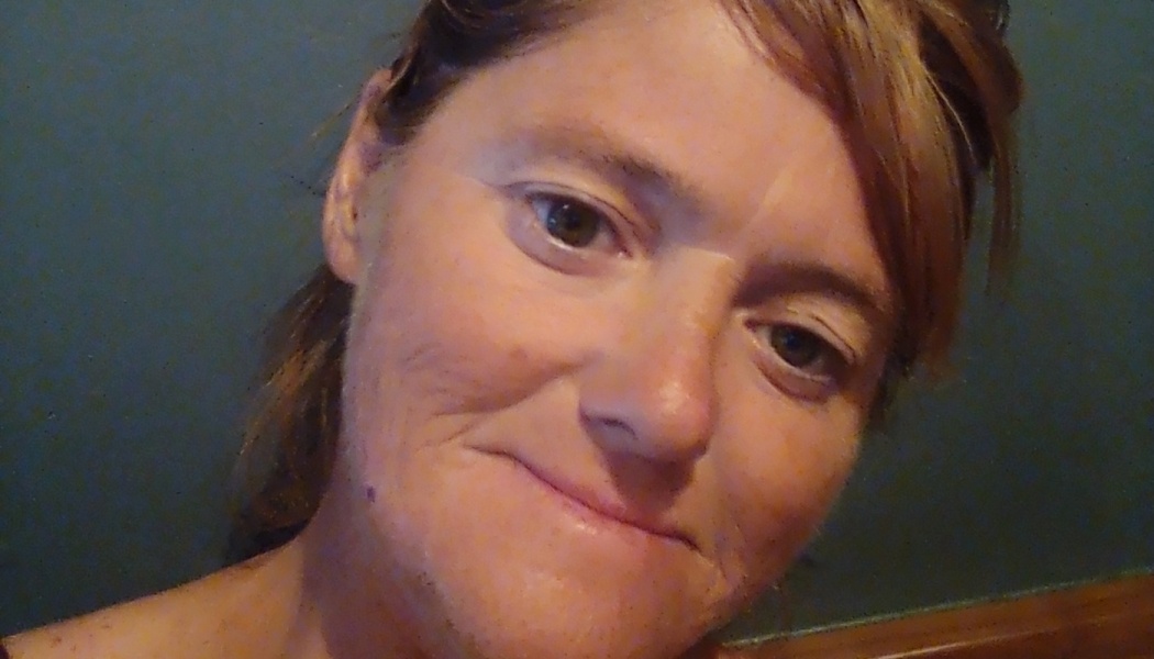 Close-up portrait of a woman with reddish-brown hair smiling gently against a dark teal background.