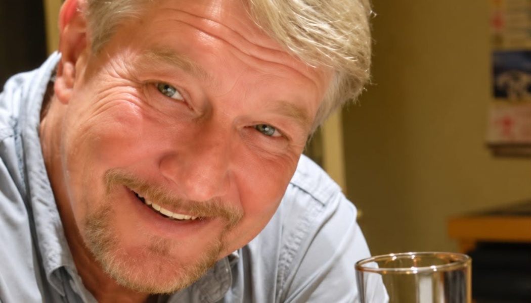 Close-up of a smiling middle-aged man with short blonde hair and a goatee, looking warmly at the camera.