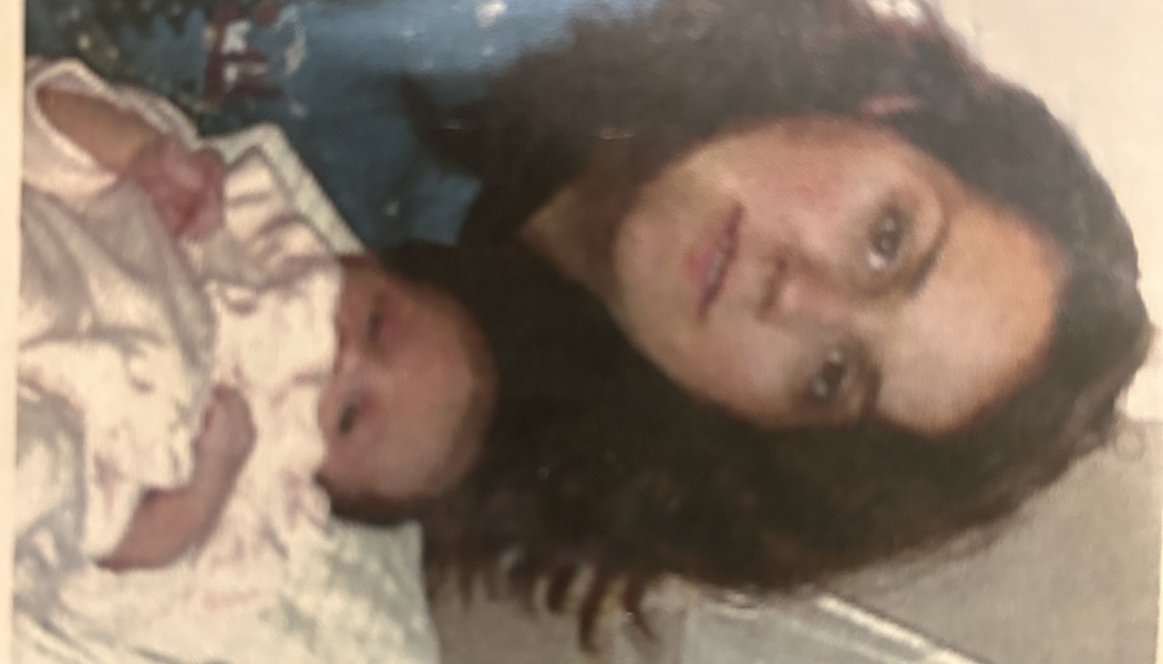 A mother with dark curly hair holds her newborn baby wrapped in a light outfit.