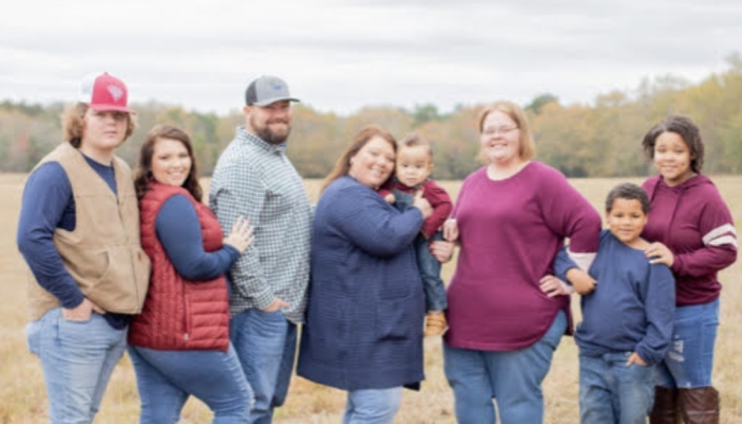 A smiling family of eight posing together outdoors in an open grassy field.