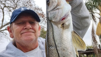 A smiling man in a blue cap proudly holding up a large caught snook fish.