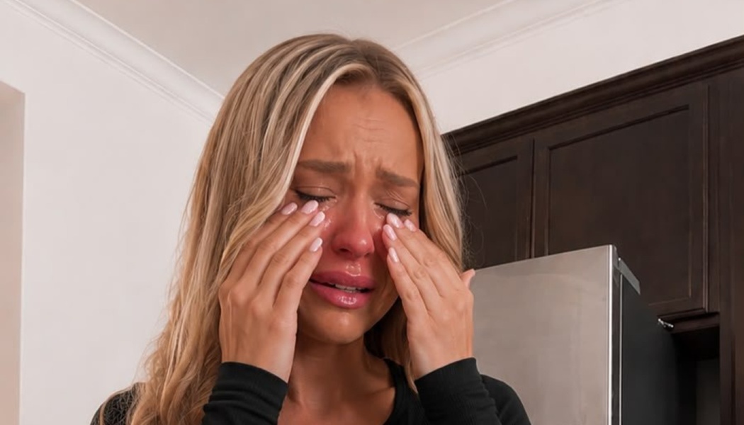 A young blonde woman crying emotionally, wiping tears from her face with both hands.
