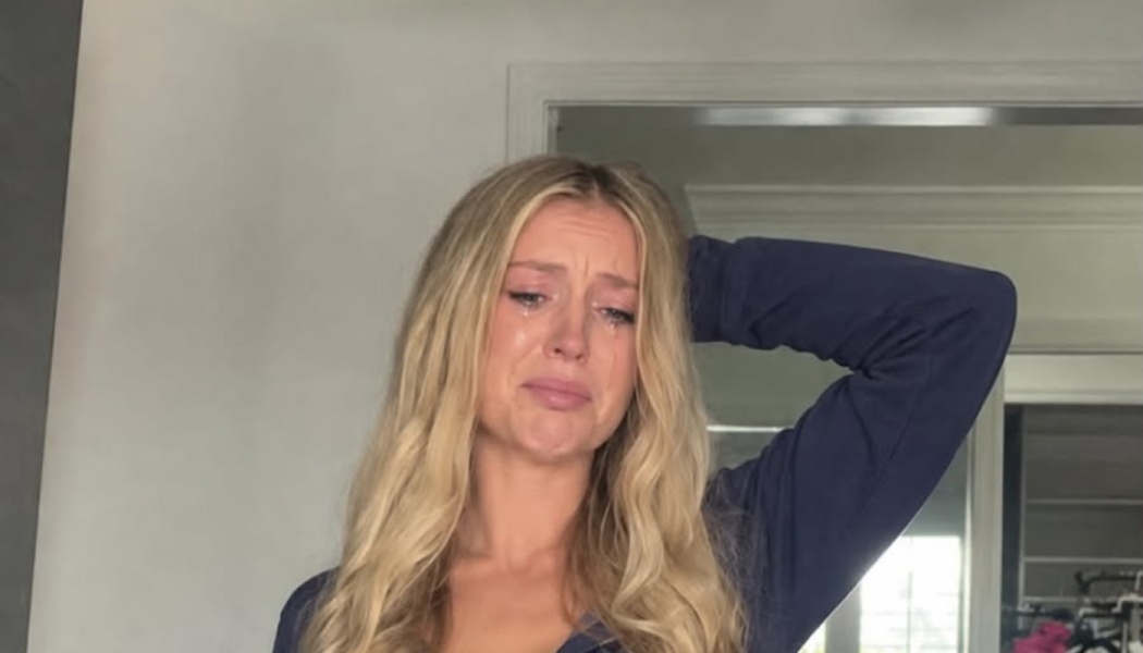 A young blonde woman crying with visible tears streaming down her face and her hand resting behind her head.