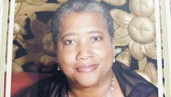 Portrait of a smiling Black woman with short gray hair, wearing pearl earrings and a necklace.