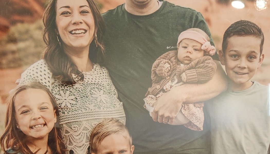 A smiling family of six posing together, including parents, three young children, and a baby.