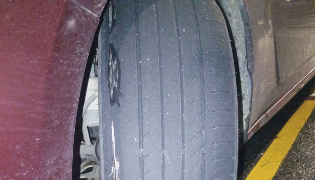 Severely worn car tire with bald tread and deep gouges along the inner edge.