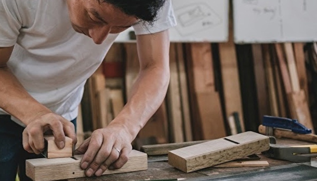 A craftsman carefully shaping a block of wood with a traditional hand plane in his workshop.