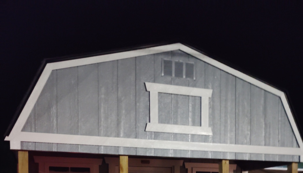 Upper front facade of a grey wooden shed featuring white trim, a decorative center frame, and gambrel roofline.