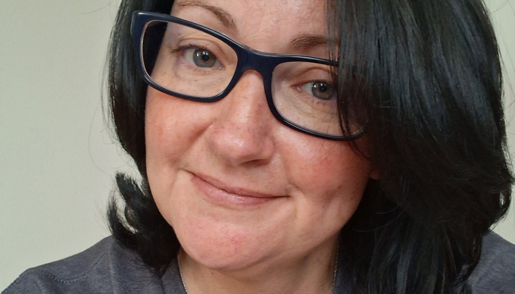 Close-up portrait of a woman with dark hair and glasses smiling softly at the camera.