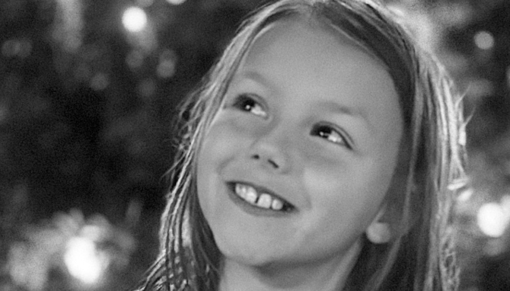 Black and white close-up of a smiling young girl looking up with a hopeful expression.