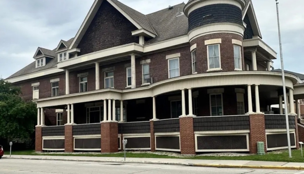 Historic multi-story brick building featuring a wrap-around porch with white columns and a round corner turret.