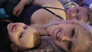 A smiling blonde woman and her two young sons cuddle close together and smile at the camera.
