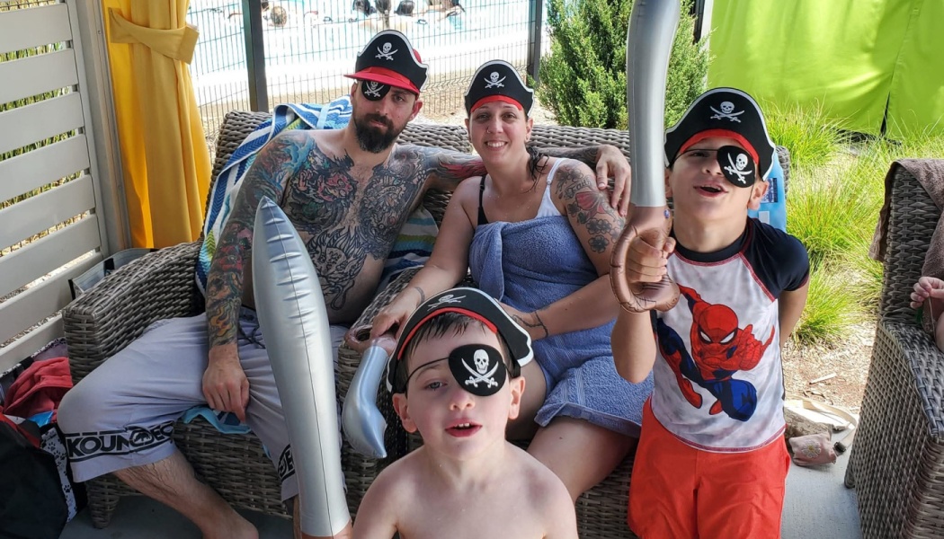 Family of four wearing pirate hats and eye patches with inflatable swords by the pool.