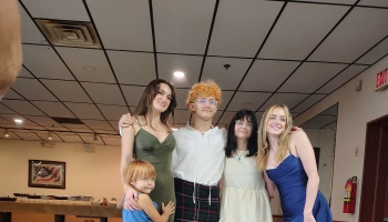 Four dressed-up young people and a child smiling together at an indoor event.