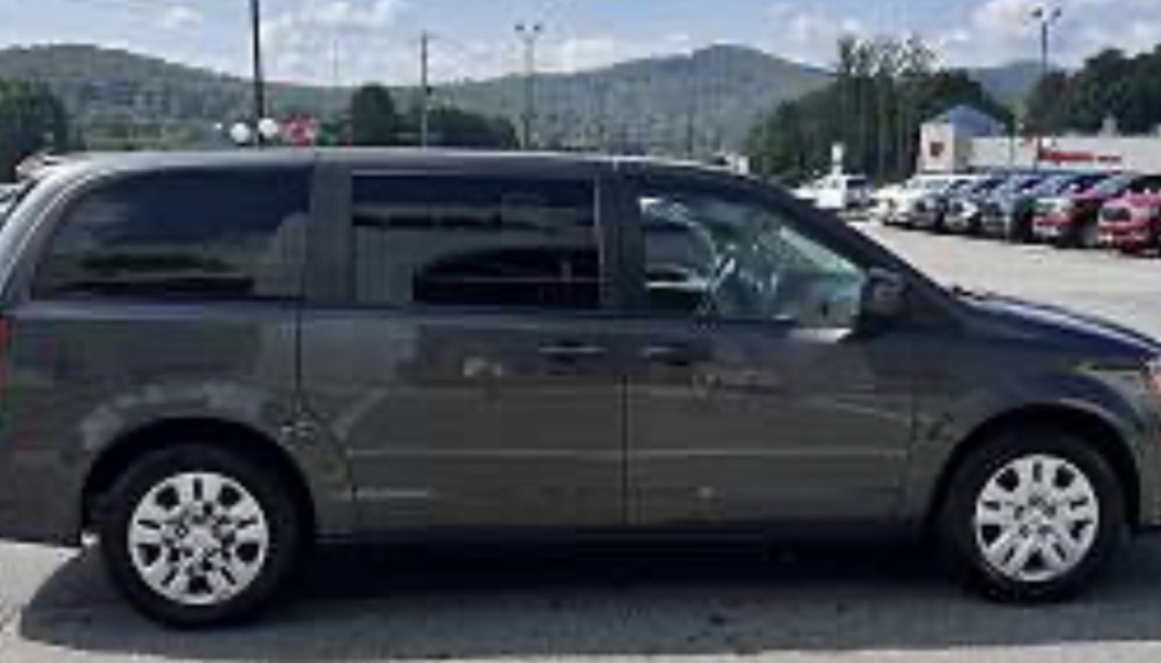 Side profile of a dark gray Dodge Grand Caravan minivan parked outdoors with mountains in the background.