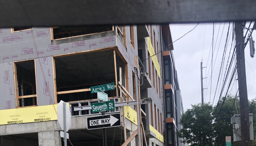 Multi-story building under construction behind street signs for Aggie's Way and Seventh St.