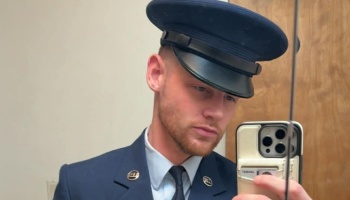 A young man in a dark blue service dress uniform and peaked cap taking a mirror selfie.
