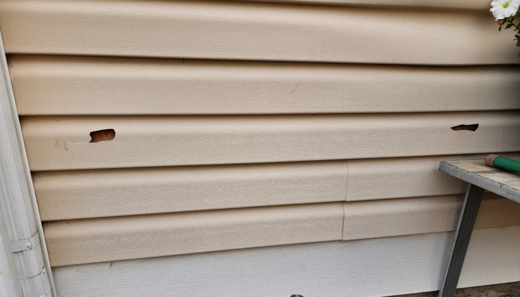 Damaged beige vinyl house siding with two small holes exposing the wall underneath.