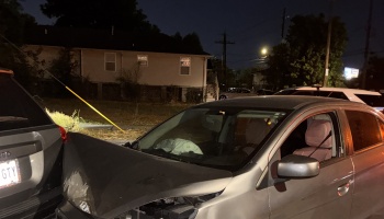Silver sedan with heavy front-end damage and a deployed airbag after crashing into the back of an SUV at night.