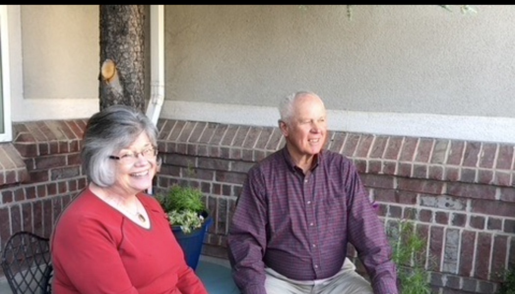 A smiling senior couple sits together outdoors on a porch.