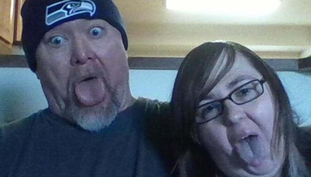 A man in a Seahawks beanie and a woman with glasses making silly faces with their tongues sticking out.