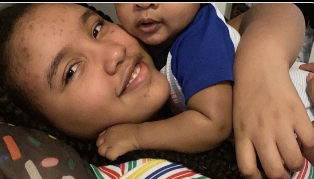 A smiling young woman lies down while warmly cuddling a baby on her chest.