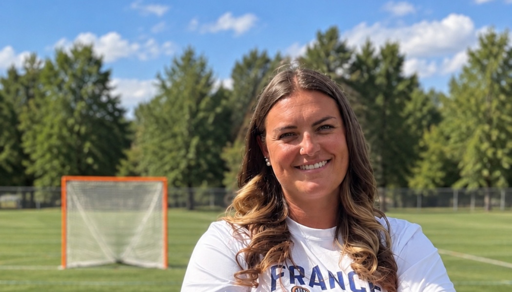 A smiling woman in a white France shirt stands on a lacrosse field with an orange net behind her.