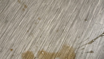 Spilled brown liquid and droplets pooling on a light grey textured wood-grain surface.