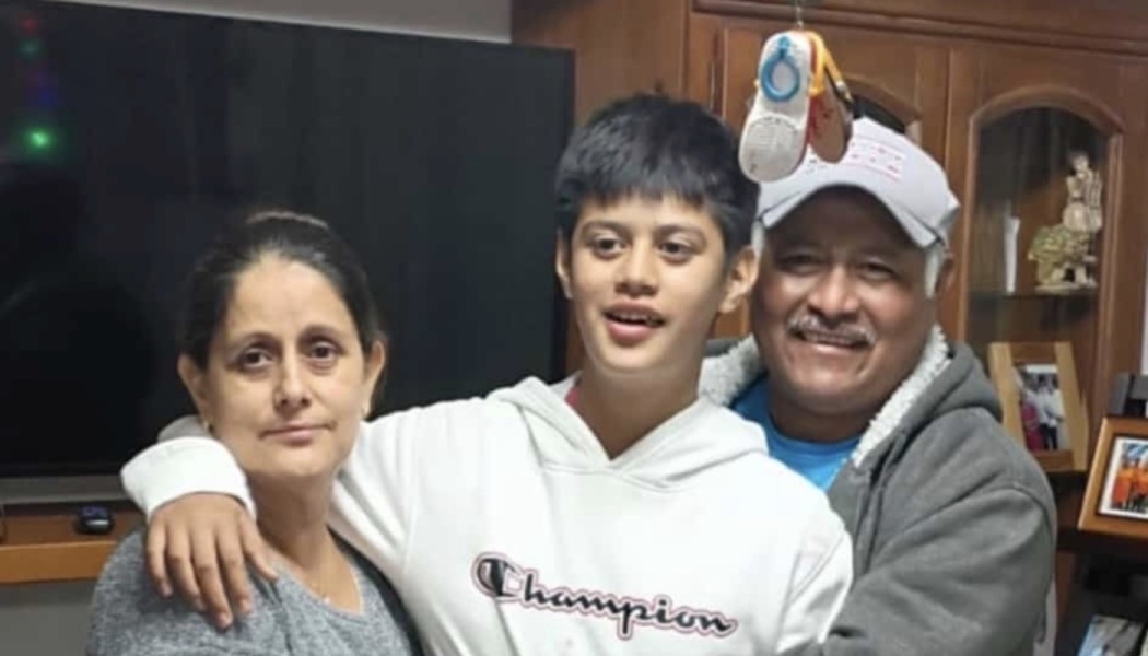 A smiling boy in a white Champion hoodie poses in a close embrace with his mother and father.