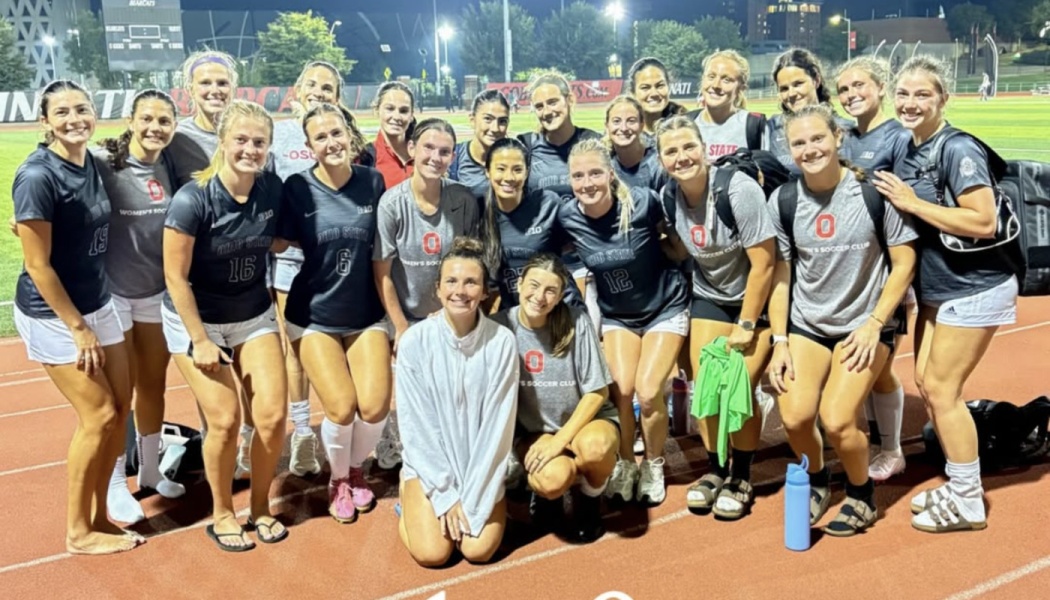 Ohio State women's soccer club team smiling together on an outdoor running track at night.
