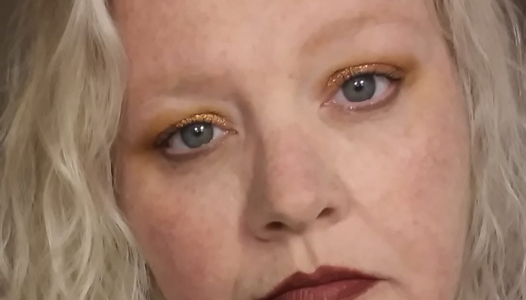 Close-up of a woman with curly blonde hair, gold glitter eyeshadow, and dark red lipstick.