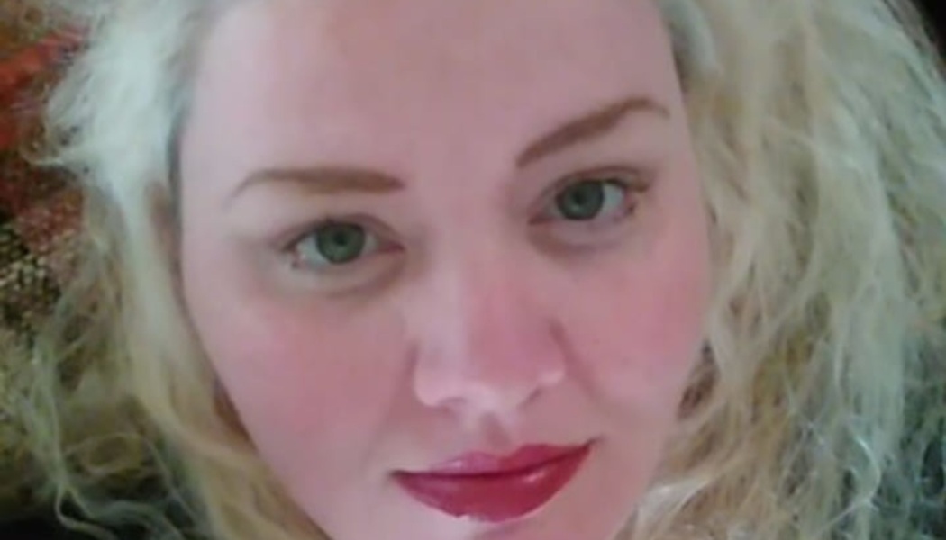 Close-up portrait of a woman with blonde hair, green eyes, and red lipstick looking directly at the camera.
