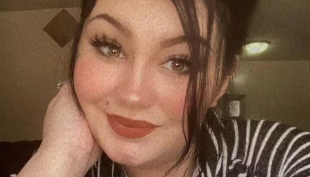 Close-up portrait of a smiling woman with dark hair and red lipstick resting her cheek on her hand.