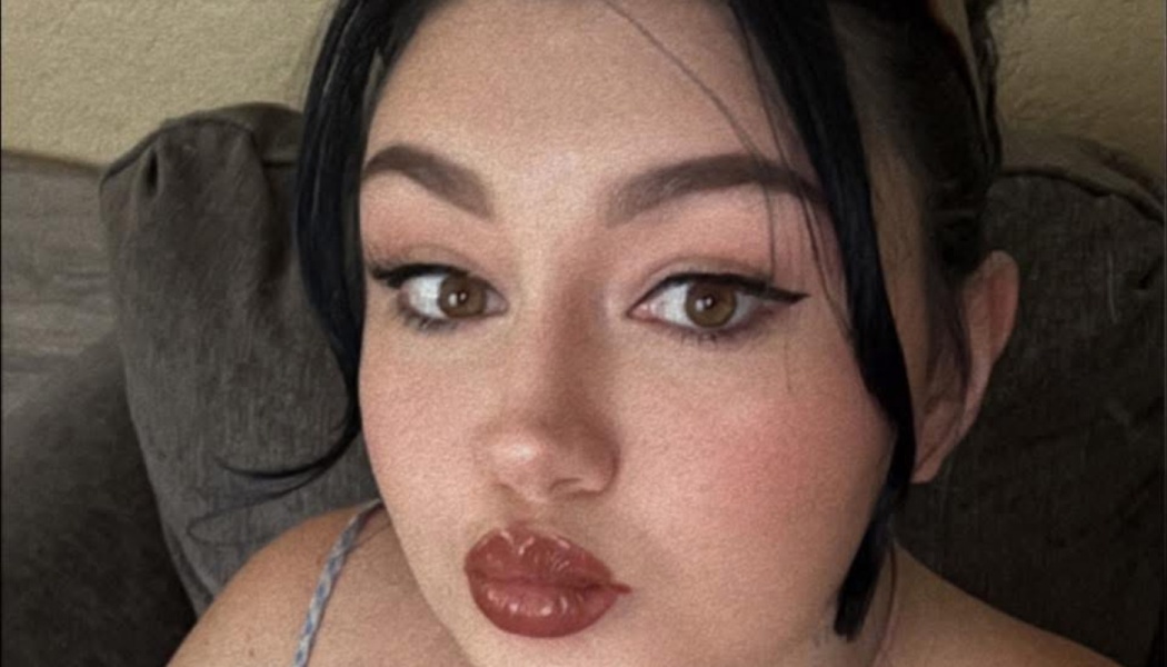 Close-up portrait of a young woman with dark hair, brown eyes, winged eyeliner, and glossy lips.