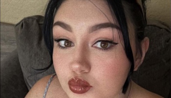 Close-up portrait of a young woman with dark hair, brown eyes, winged eyeliner, and glossy lips.