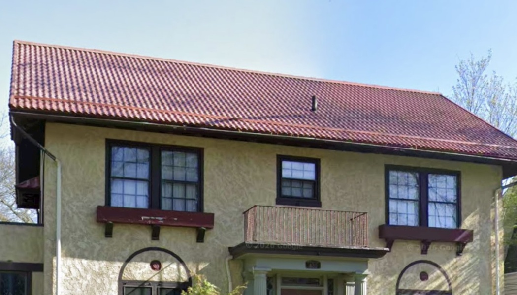 A two-story tan stucco home featuring a red tile roof, dark-framed windows with window boxes, and a central balcony.