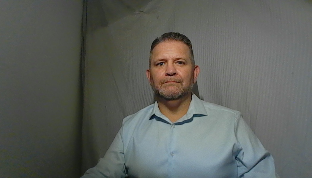 A middle-aged man with a short beard wearing a light blue button-down shirt looking directly at the camera.