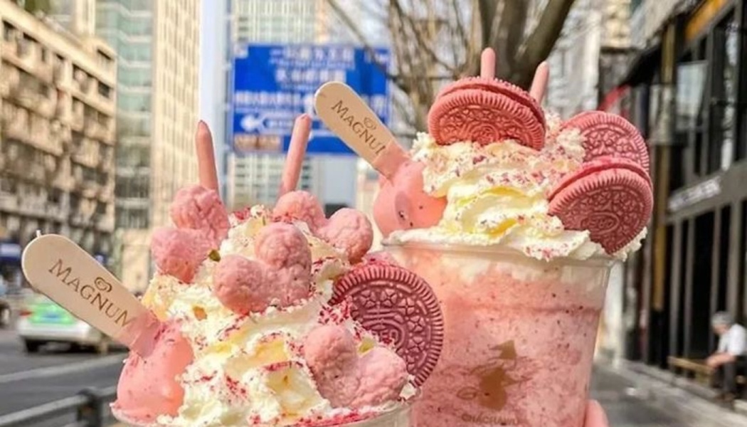 Two pink strawberry frappes topped with whipped cream, pink Oreos, and pink Magnum ice cream bars.