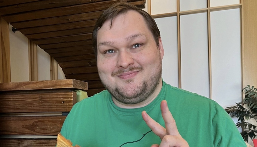 Smiling man in a green shirt giving a peace sign while holding food.