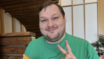 Smiling man in a green shirt giving a peace sign while holding food.