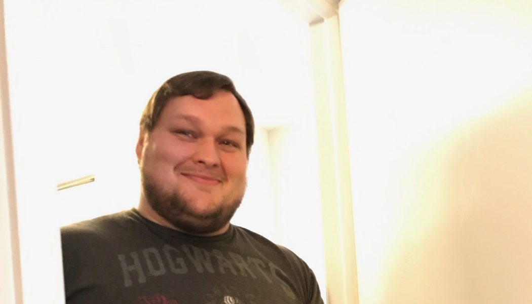 A smiling man with a beard wearing a dark Hogwarts t-shirt standing in a doorway.