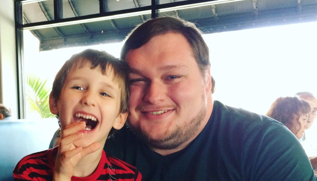 A smiling man leaning next to a laughing young boy in a red and black striped shirt.