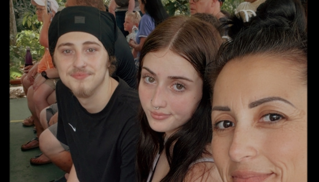 A woman takes a selfie with a young man wearing a black beanie and a young woman with dark hair.